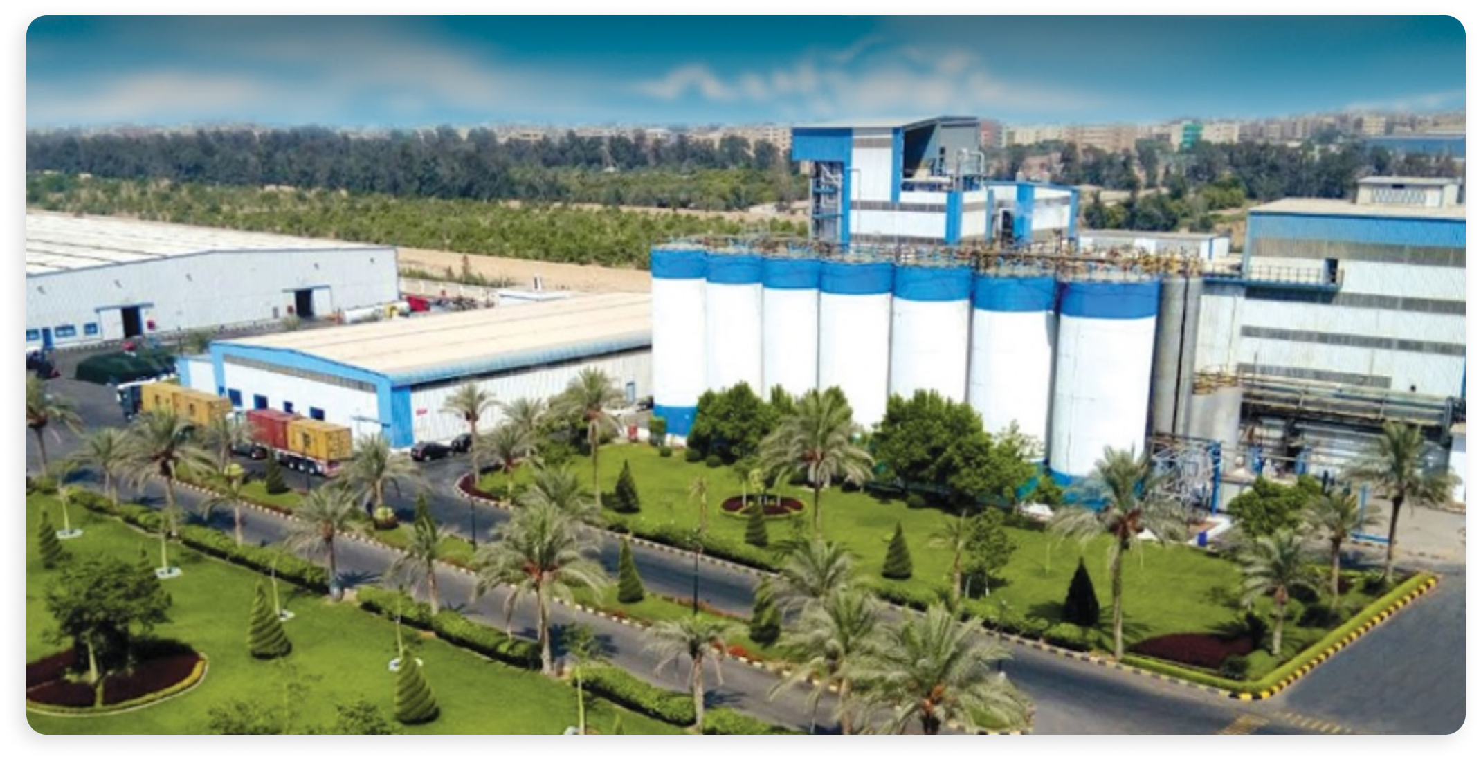 The image depicts a factory with multiple building and a city in the background.